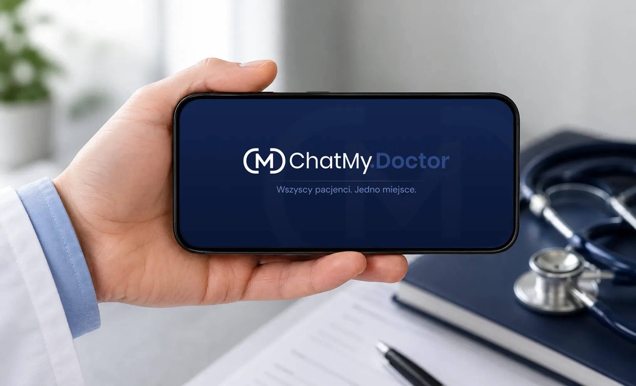 Telefon w dłoni lekarza z poziomą wersją logo ChatMy.Doctor na granatowym ekranie startowym, z hasłem „Wszyscy pacjenci. Jedno miejsce.”