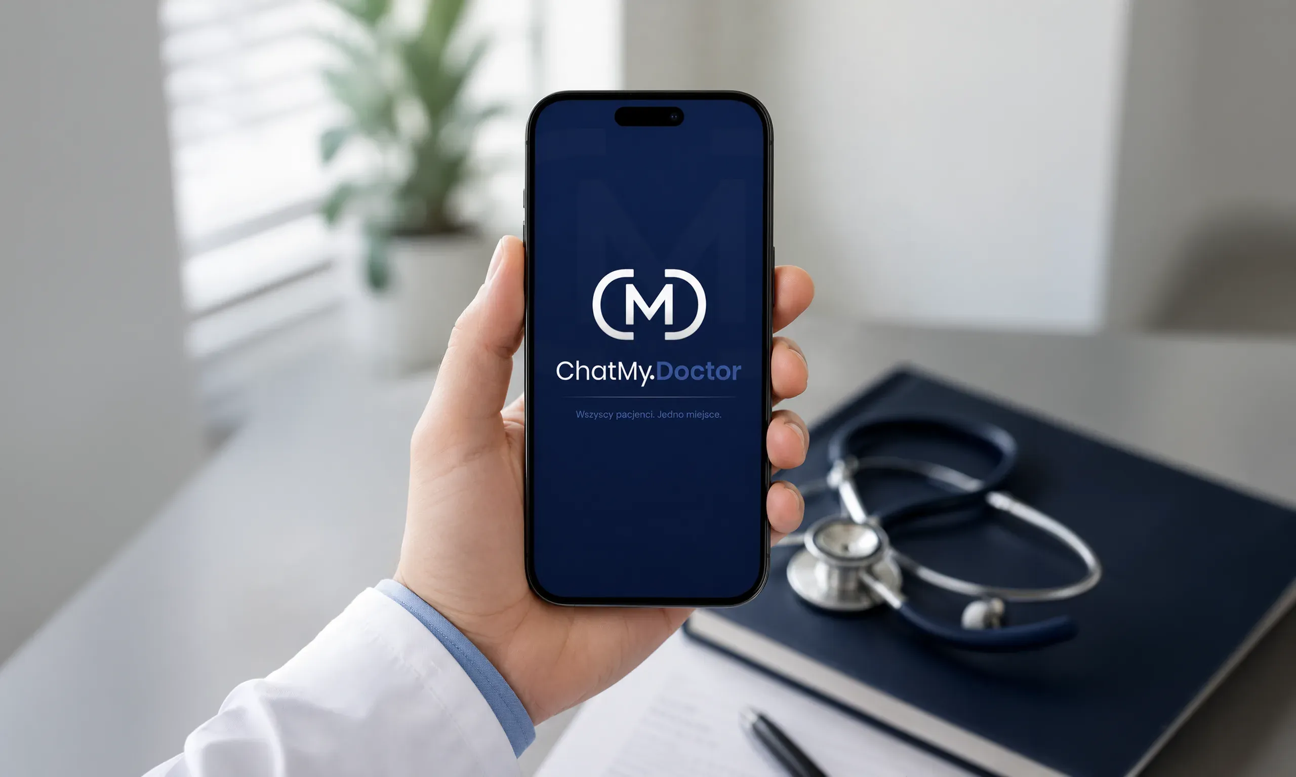 Telefon w dłoni lekarza z pionową wersją logo ChatMy.Doctor – sygnet nad nazwą – na granatowym ekranie startowym