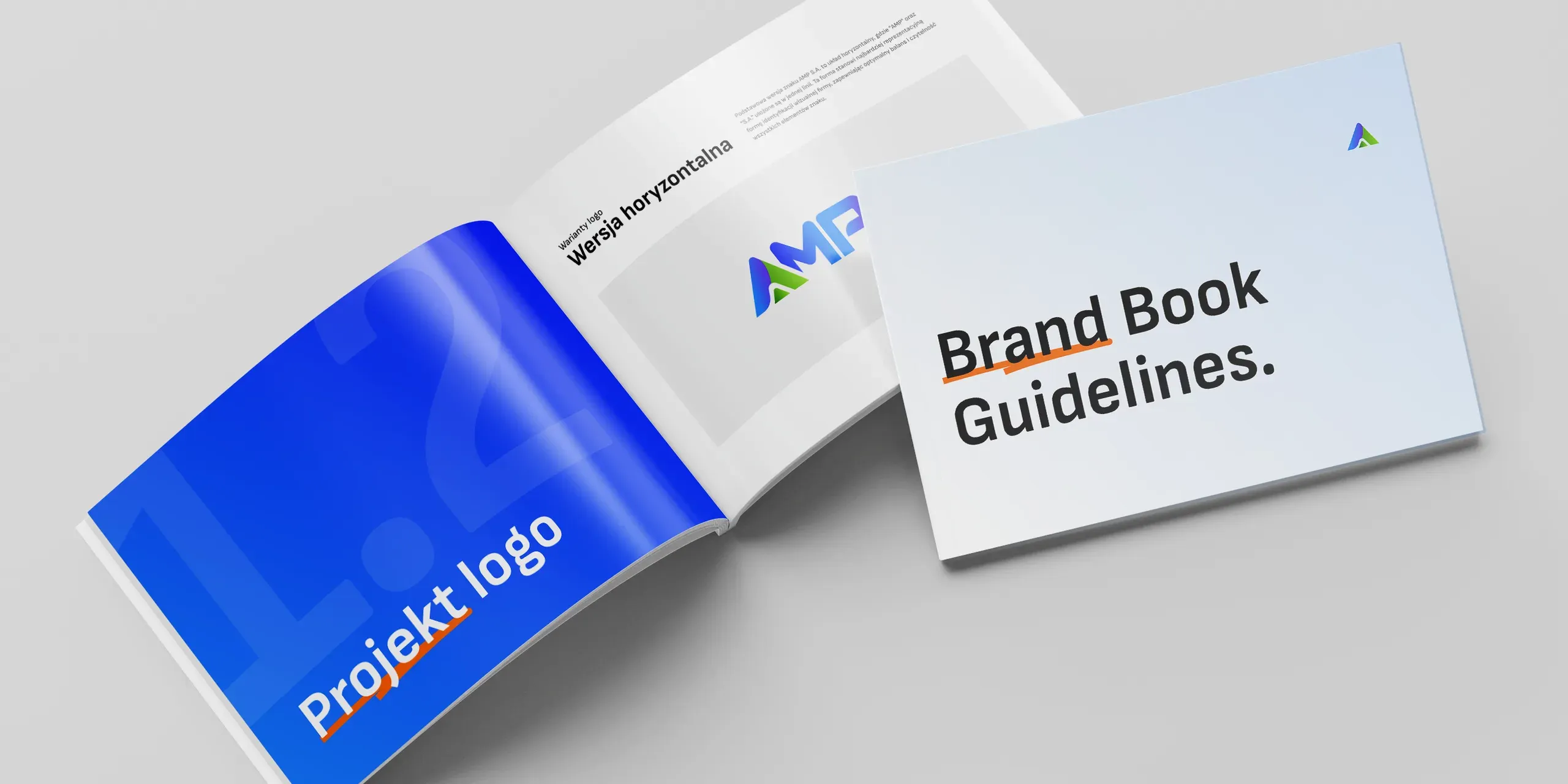 Dwa egzemplarze brandbooka AMP S.A. na jasnym blacie: okładka „Brand Book Guidelines” i rozłożony rozdział „Projekt logo” z niebieską stroną tytułową.